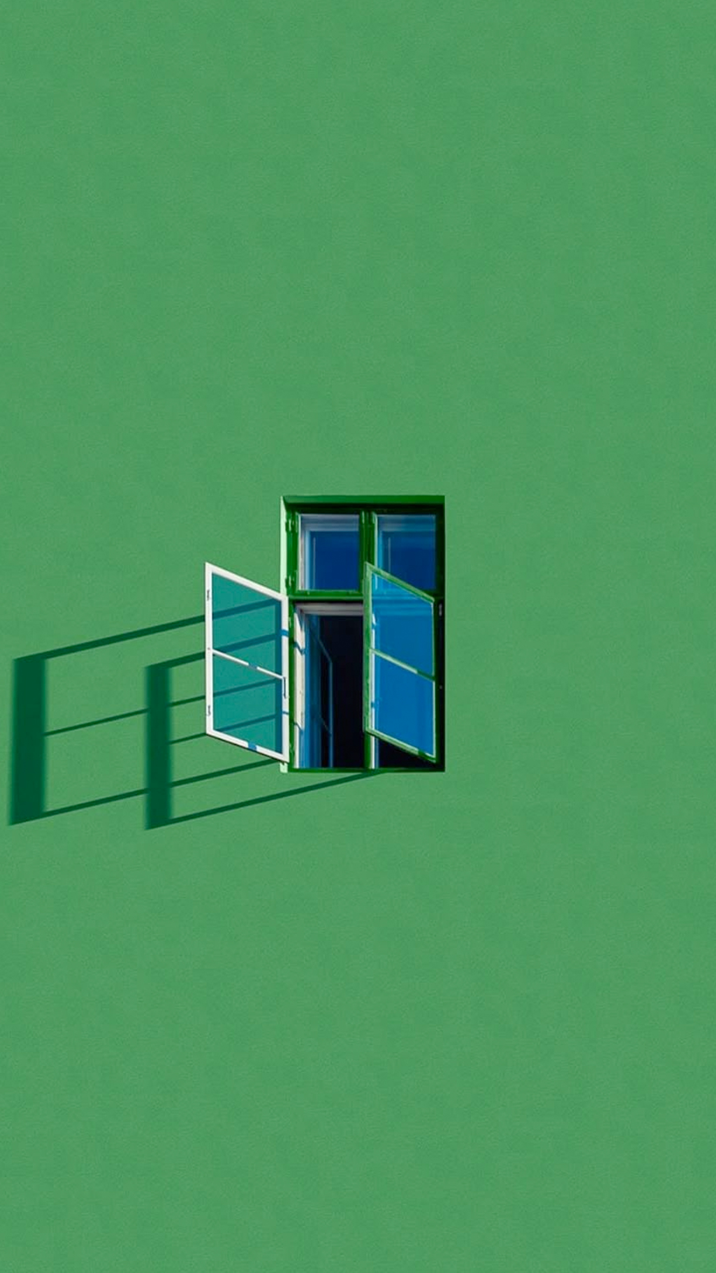 A window with open shutters casts a shadow against a vibrant green wall.