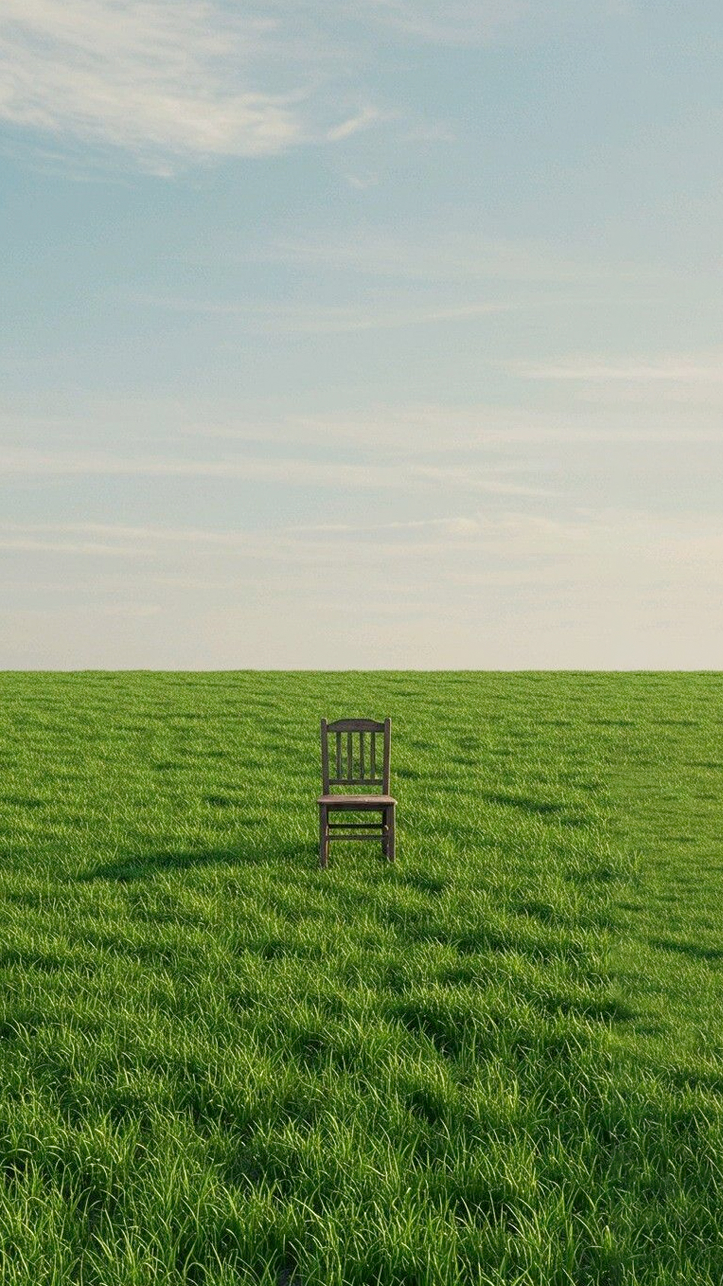 A solitary wooden chair sits amidst a vast, expansive grassy field.
