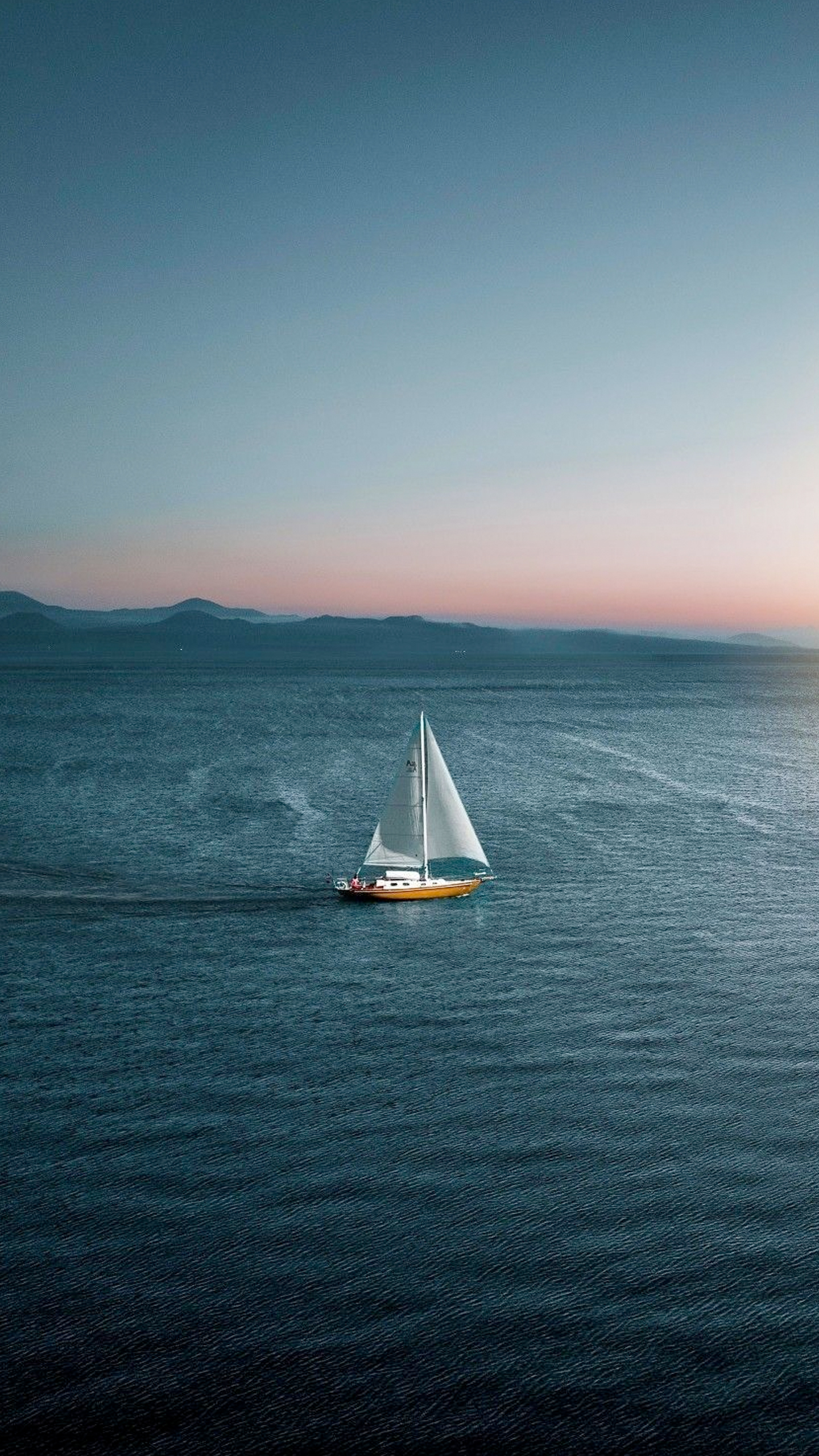 A small sailboat glides across the vast ocean, its white sails billowing in the breeze.
