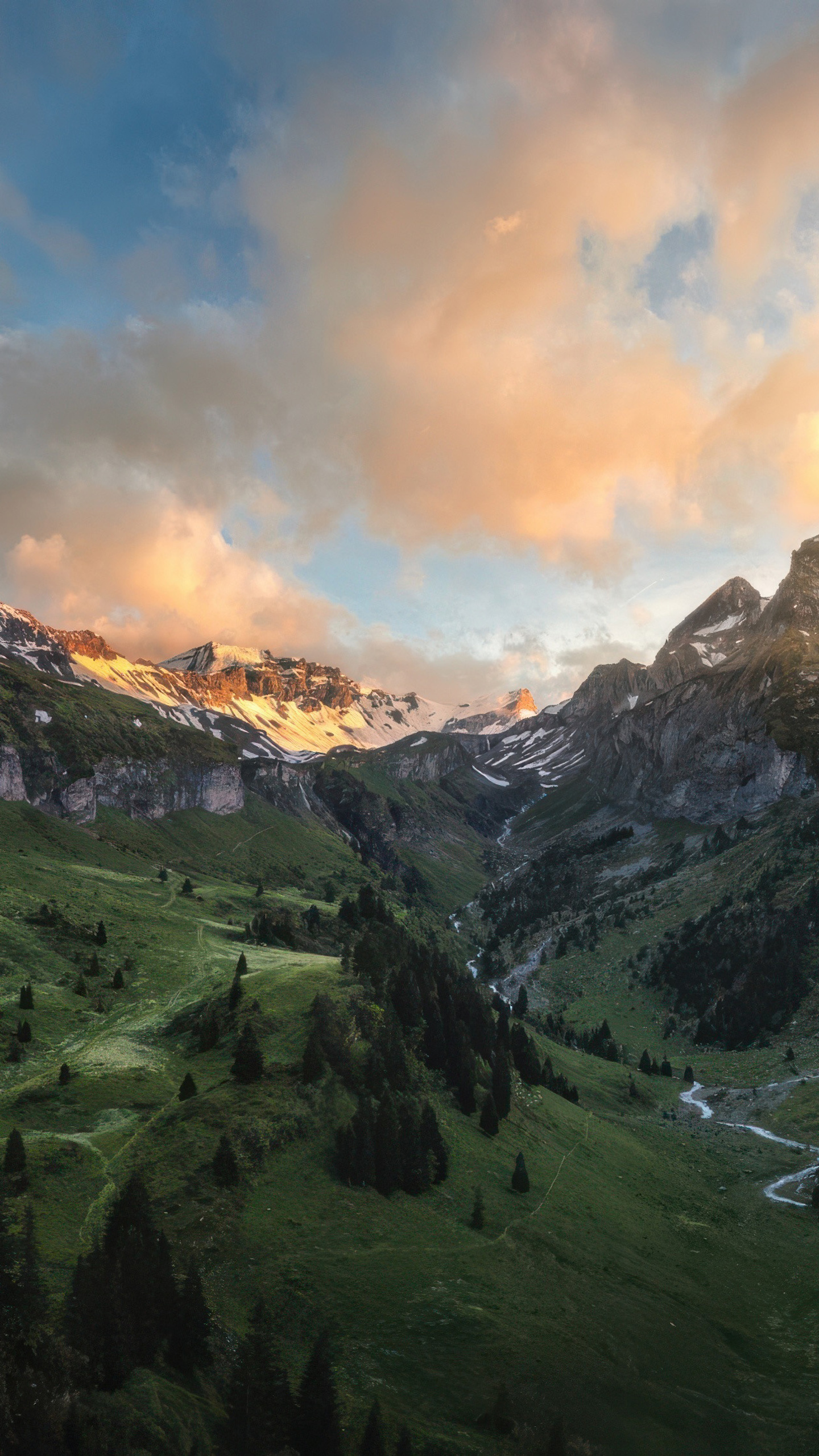 Snow-capped mountains meet lush green valleys under a cloudy sky.