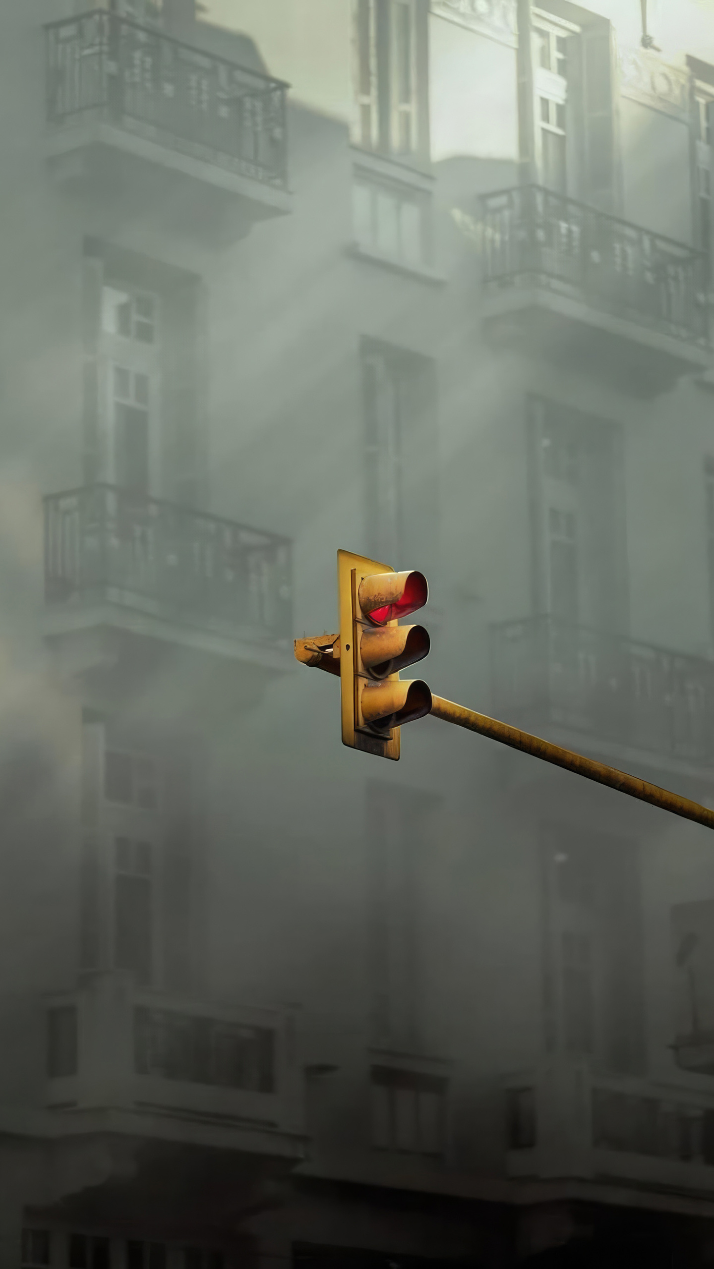 A weathered yellow traffic light stands out against a backdrop of misty, foggy buildings with balconies.