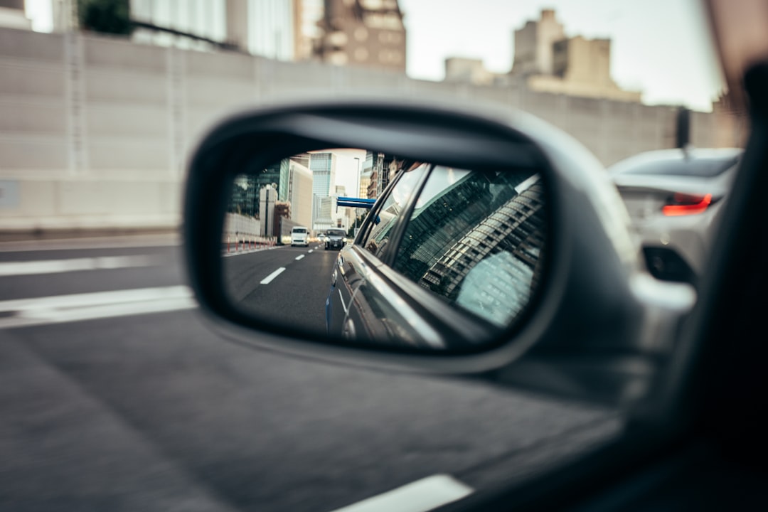 A city street scene is reflected in the rearview mirror of a car, with buildings and vehicles visible.