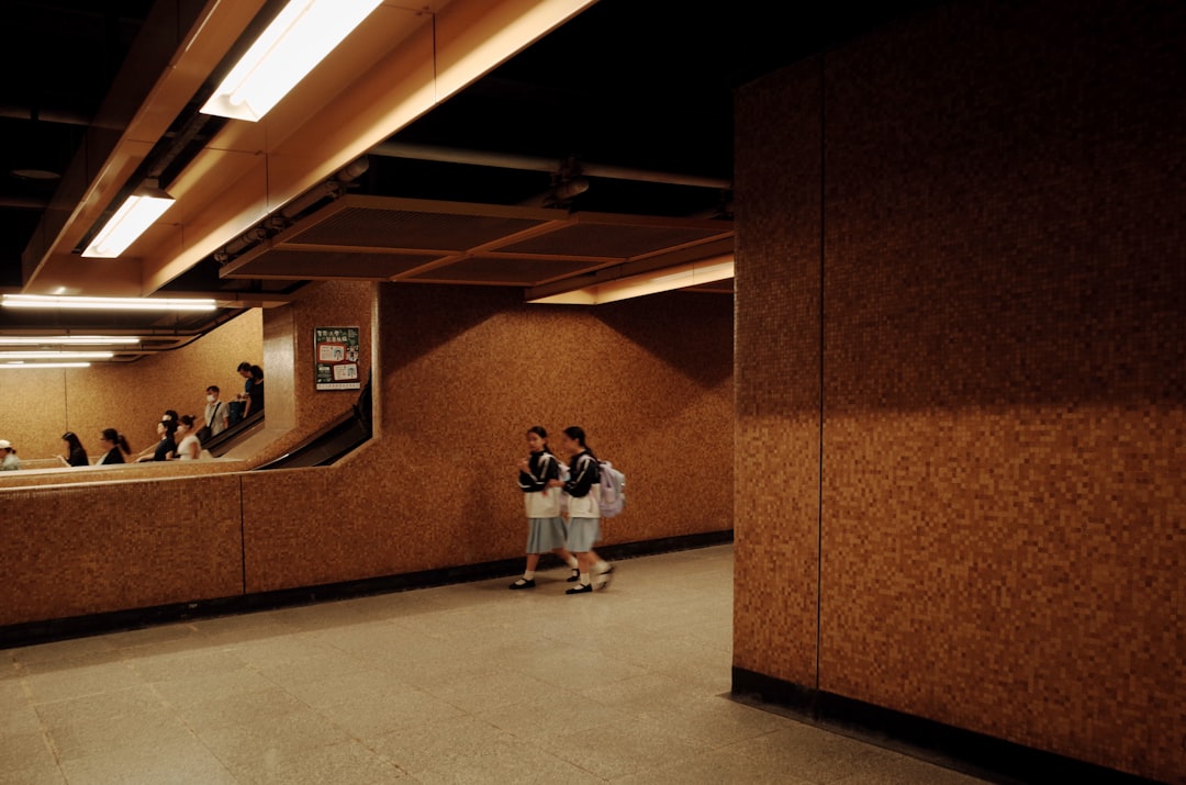 Two schoolgirls walk through a dimly lit underground area with brown walls and fluorescent lights.