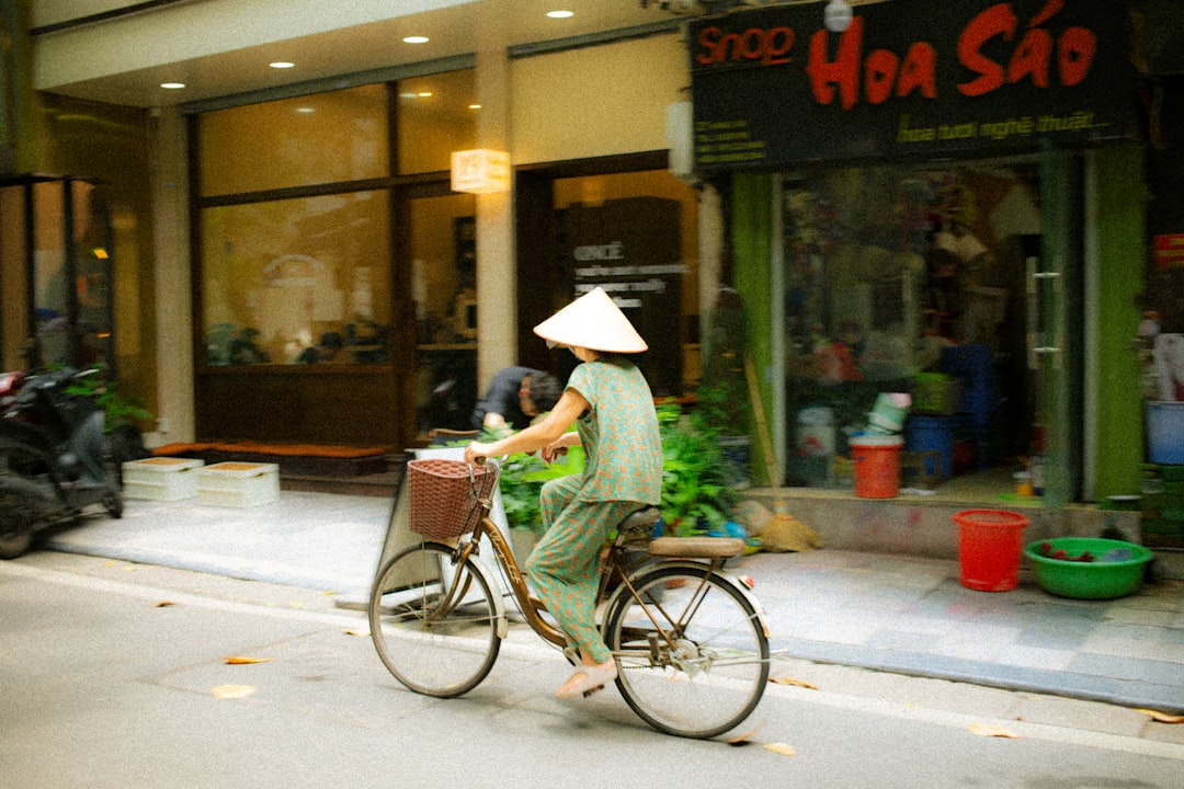 A woman in a conical hat rides a bicycle on a street.