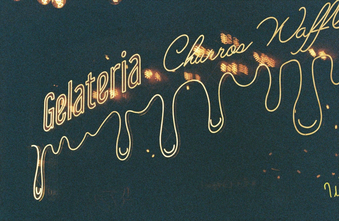 Golden letters adorn a dark background, spelling out "Gelateria Churros Waffles" in elegant cursive.