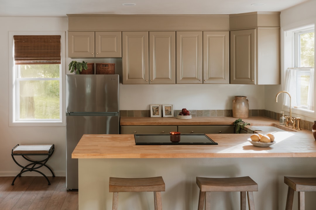 A sleek stainless steel refrigerator stands alongside a matching stove top, nestled within a kitchen adorned with light-colored cabinets and a warm wooden countertop.