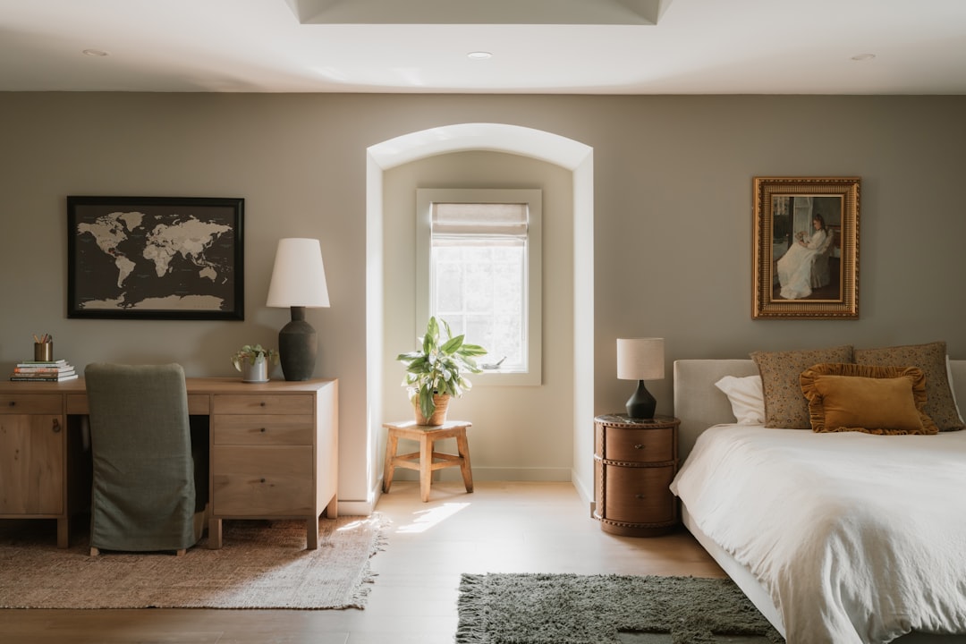 Soft sunlight illuminates a serene bedroom scene, with a white bed and desk in the foreground.