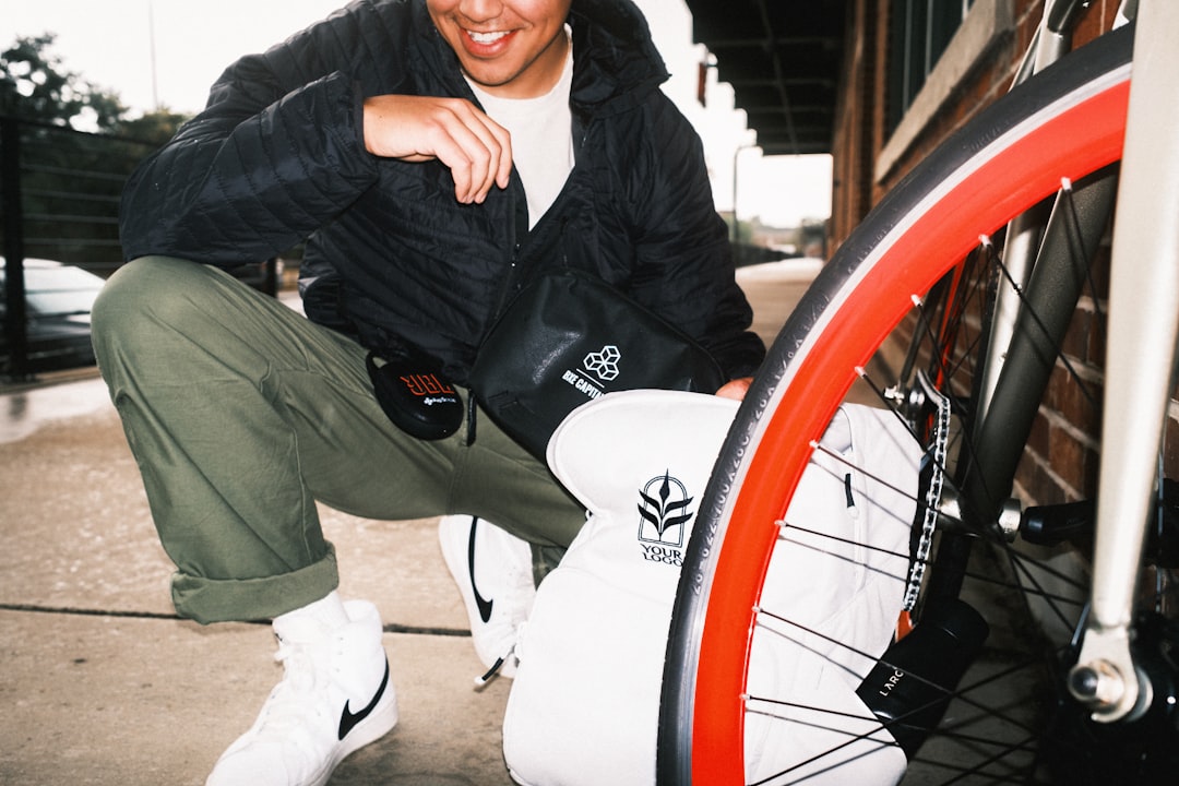 A person in a black jacket, crouching next to a bicycle with a red wheel.