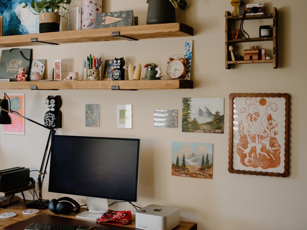 A wooden desk is situated in front of a wall adorned with various paintings and artwork, accompanied by a computer monitor and keyboard.