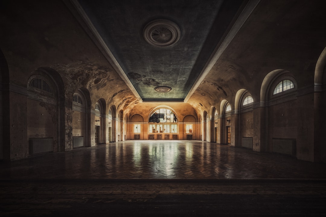 Sunlight illuminates a spacious room with arched windows and a high ceiling.