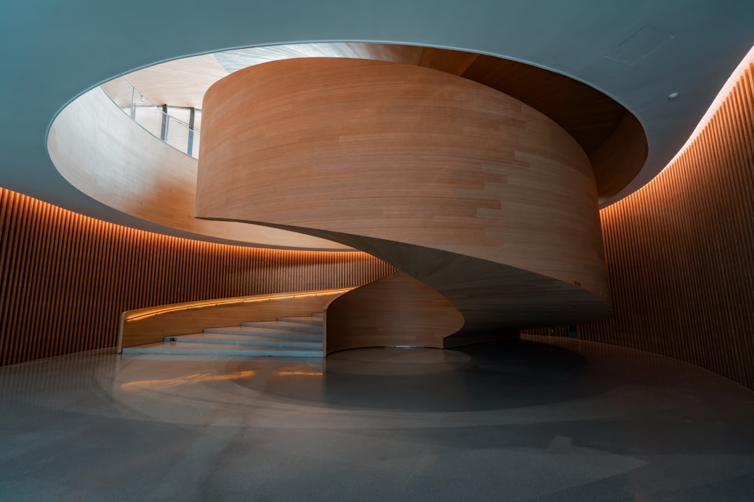 A large, curved wooden staircase dominates the space, its light-colored wood contrasting with the darker walls and floor.
