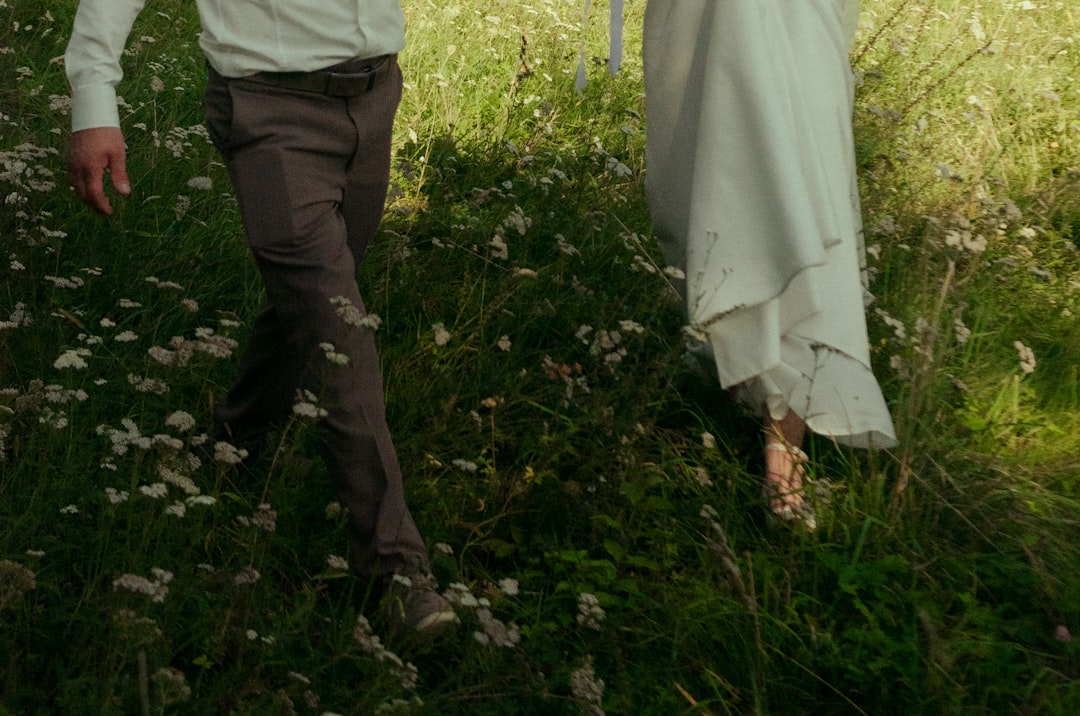 A couple walks hand in hand through a field of wildflowers.