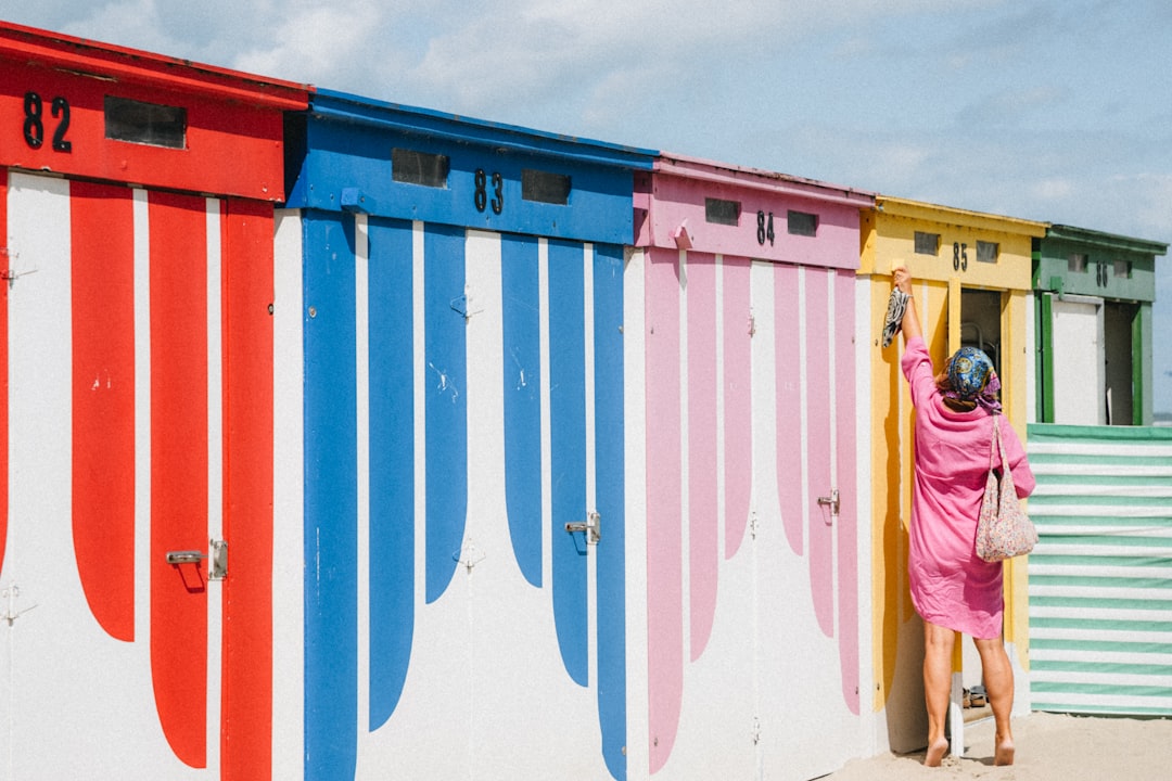 A woman in a pink dress reaches for a door on a row of colorful beach huts.