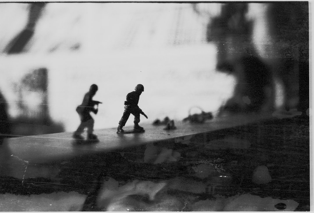 Two toy soldiers walk across a table, their miniature forms silhouetted against a blurred background.