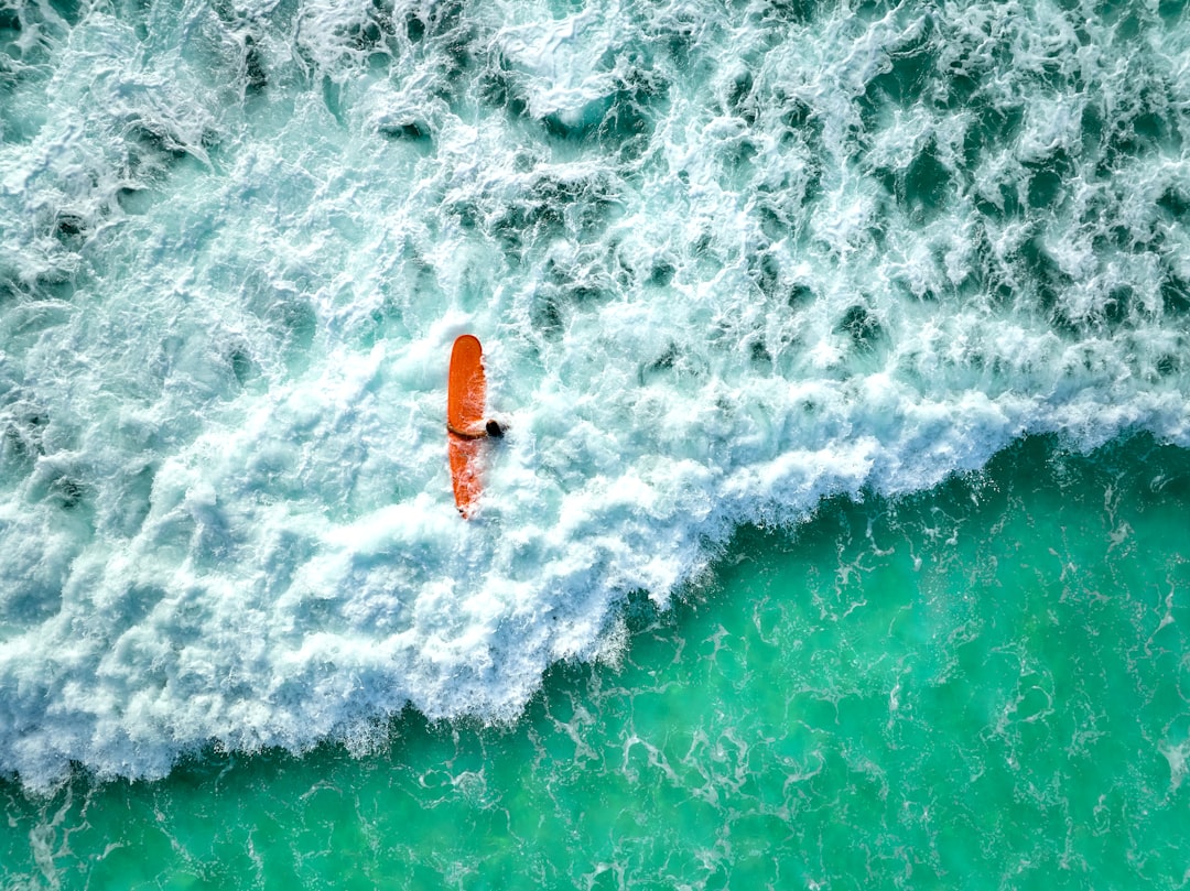 A lone orange surfboard navigates through a sea of turquoise waves.