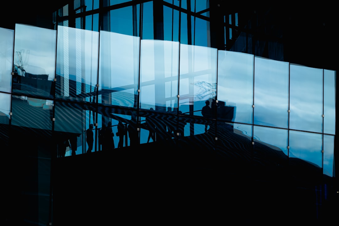 People's silhouettes are reflected in the curved glass panels of a building.