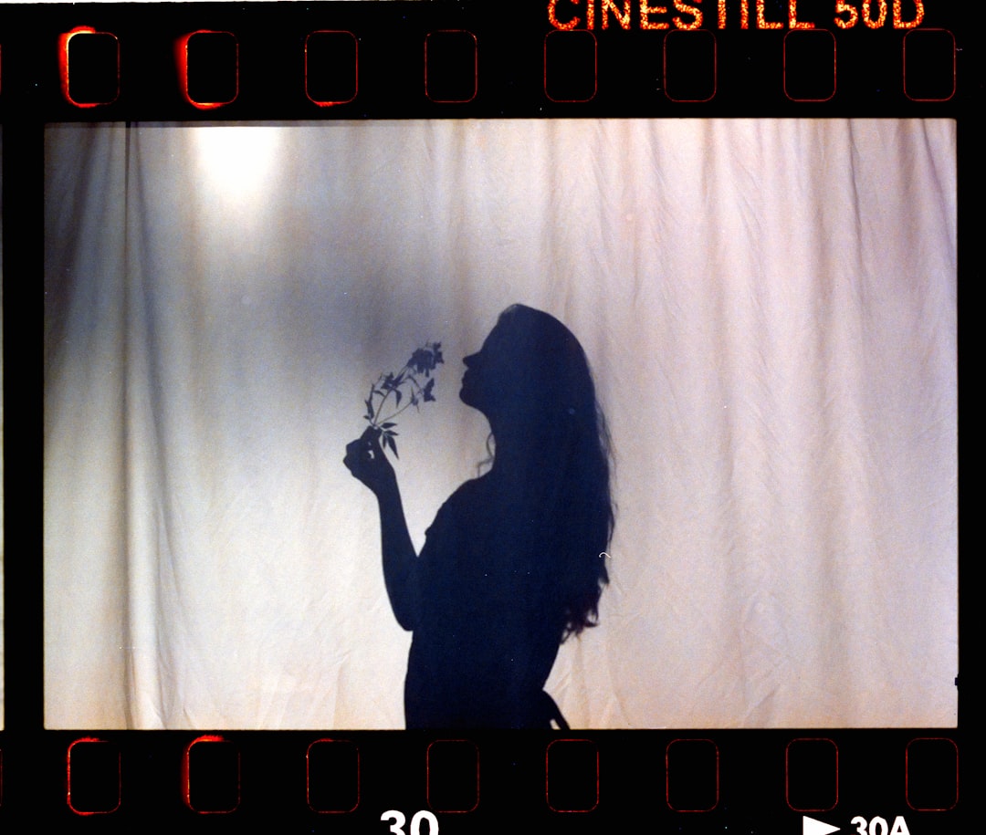 A woman with long hair stands in front of a white curtain, holding a plant.
