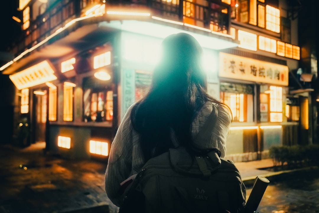 A woman stands in front of a building with a vibrant neon-lit facade.