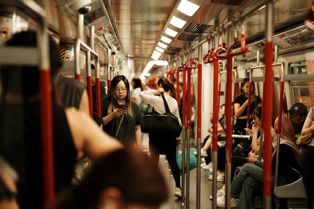 A train car filled with people, featuring red poles and a silver ceiling.