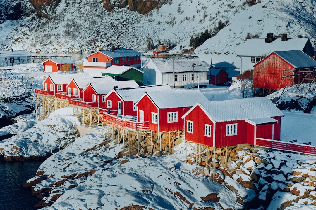 Snow-covered red houses line the rocky shore, nestled among the mountains.