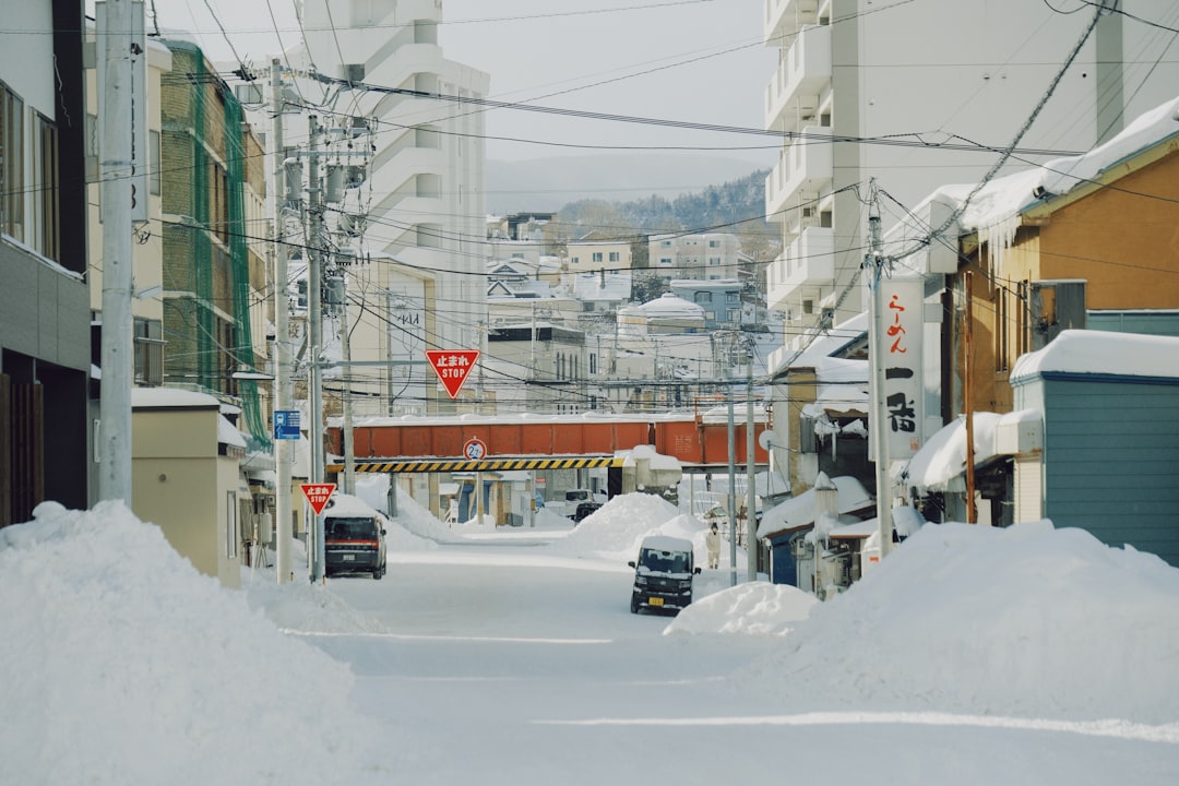 Snow-covered city street with cars and buildings, featuring red stop signs.