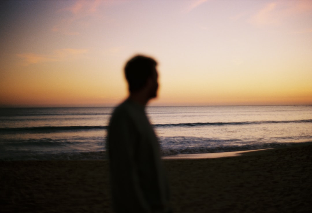 A man stands on a beach at sunset, his silhouette stark against the vibrant sky.