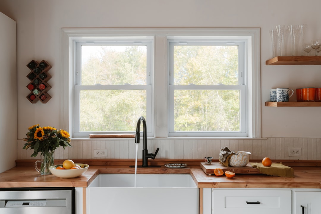 A kitchen sink sits under a window, surrounded by a countertop adorned with a vase of sunflowers and a bowl of fruit.