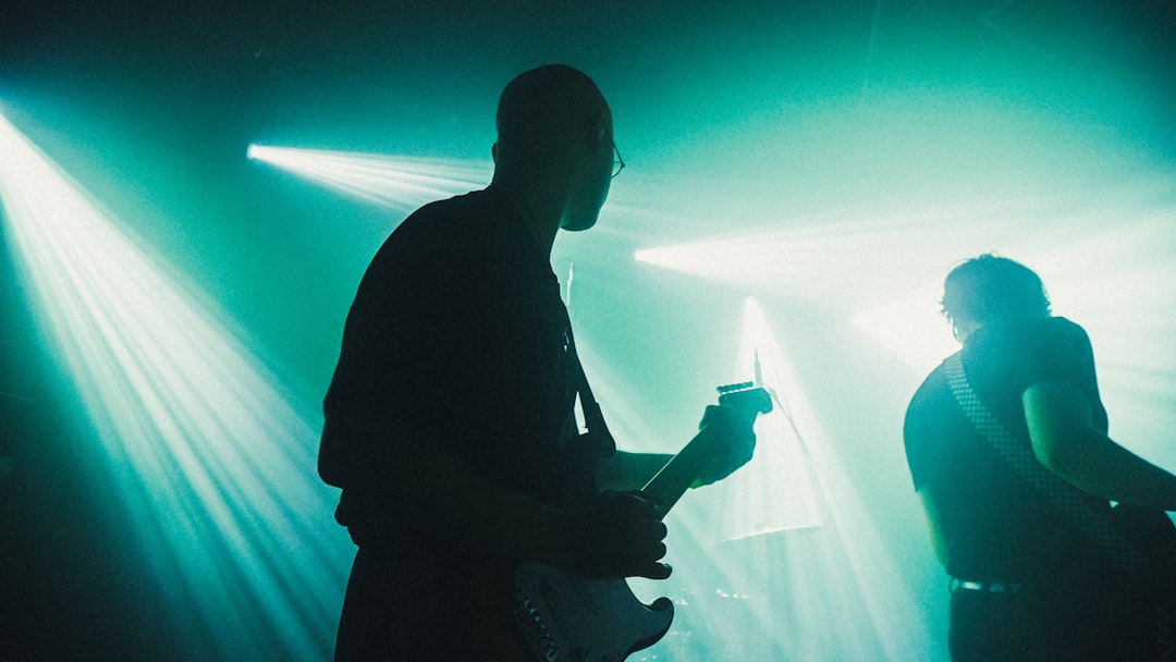 A man is playing an electric guitar under green stage lights.