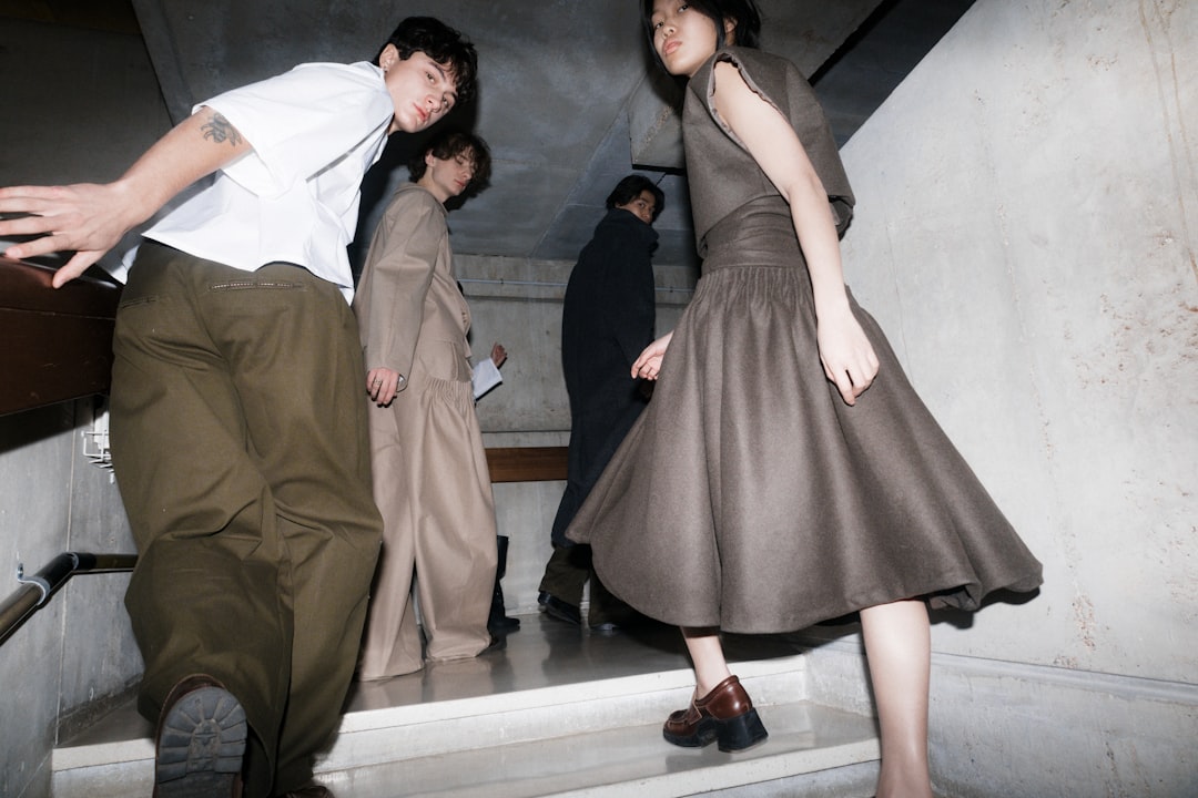 A group of four individuals, dressed in earthy tones, descend a concrete staircase, their attire blending harmoniously with the industrial backdrop.