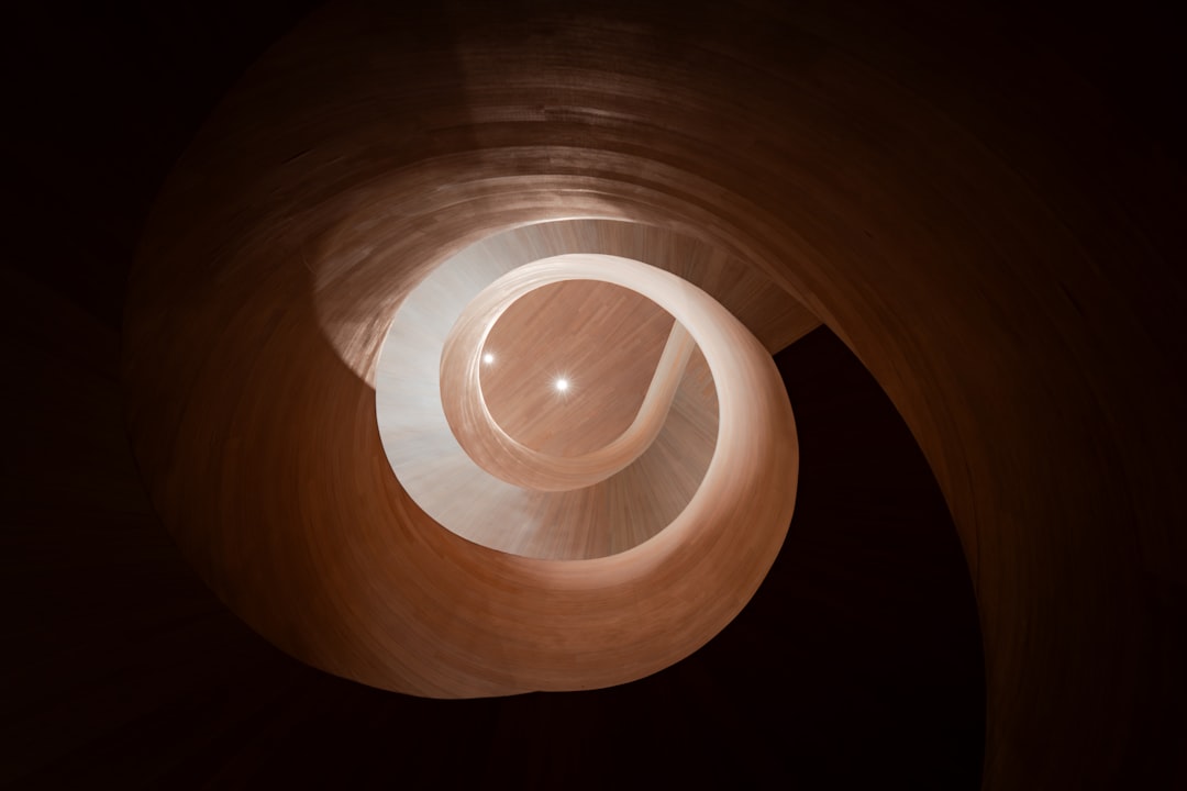 A spiral staircase with a circular opening at the top, set against a dark background.