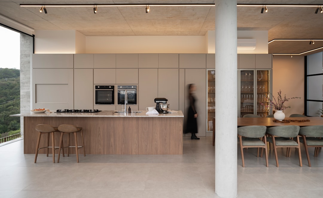 A sleek, modern kitchen with a large island and a dining area, featuring a woman in black walking through the space.
