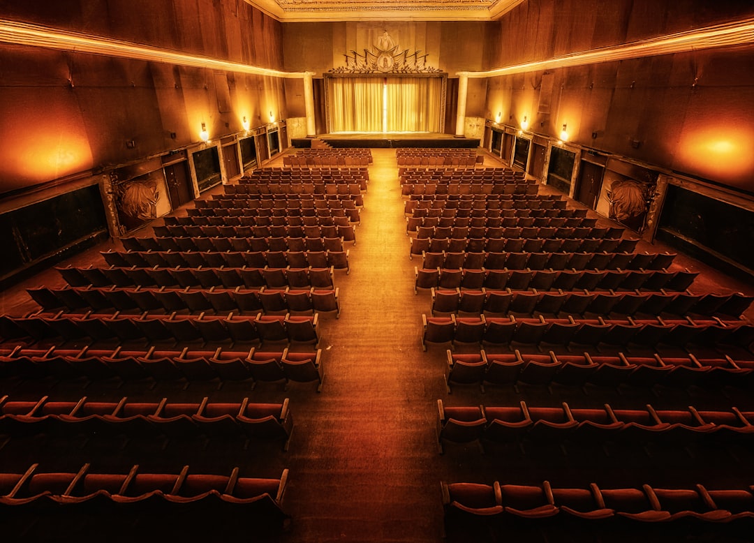 A grand theater with a majestic stage and rows of plush red seats, bathed in warm, golden light.