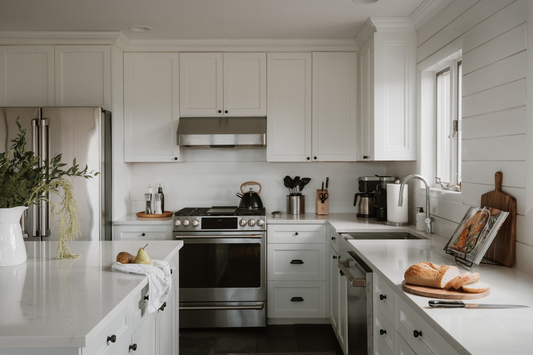 A stainless steel stove and oven sit in a sleek white kitchen, surrounded by crisp white cabinets and countertops.