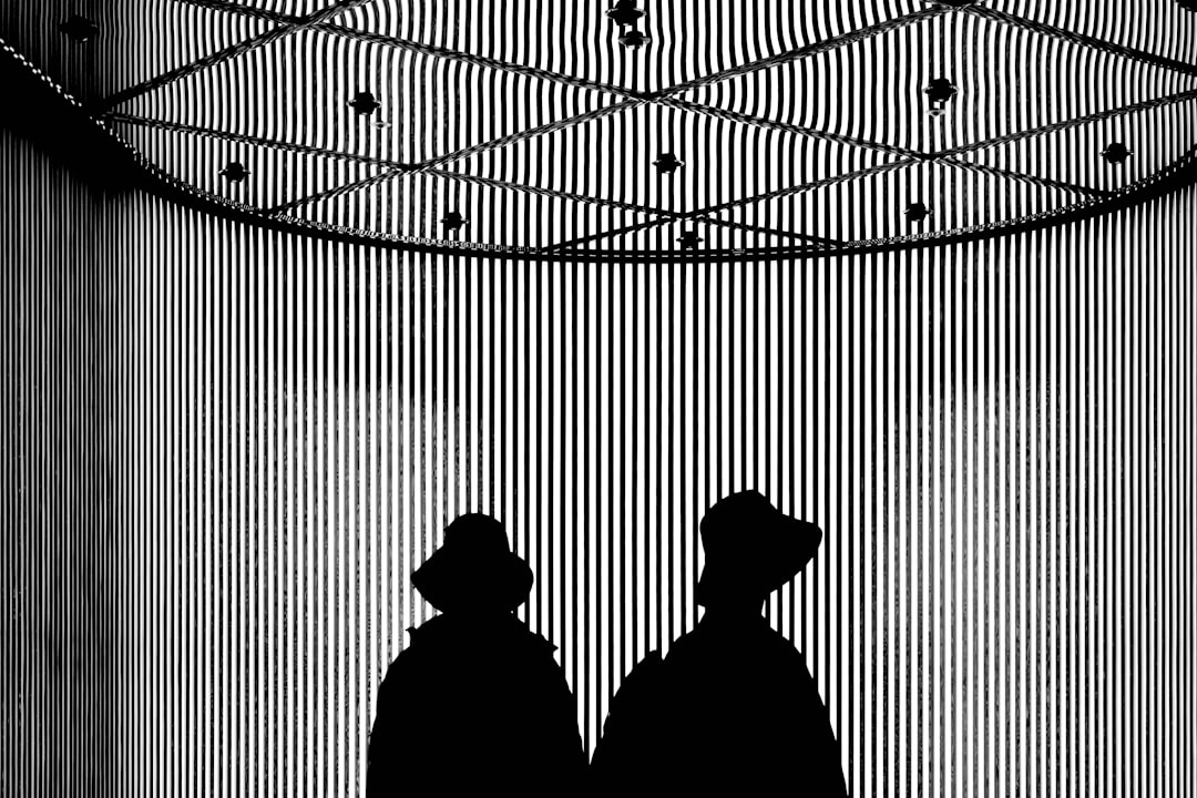 Two people stand in front of a striped wall, their silhouettes stark against the vibrant backdrop.