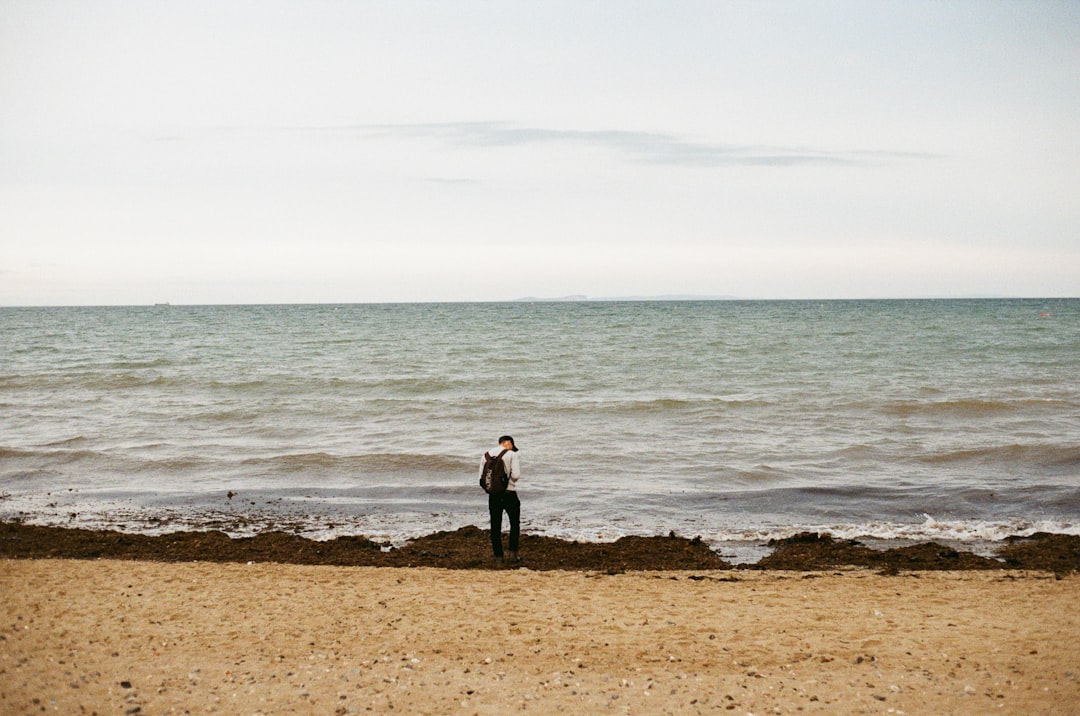 A solitary figure stands on the beach, gazing out at the vast ocean.