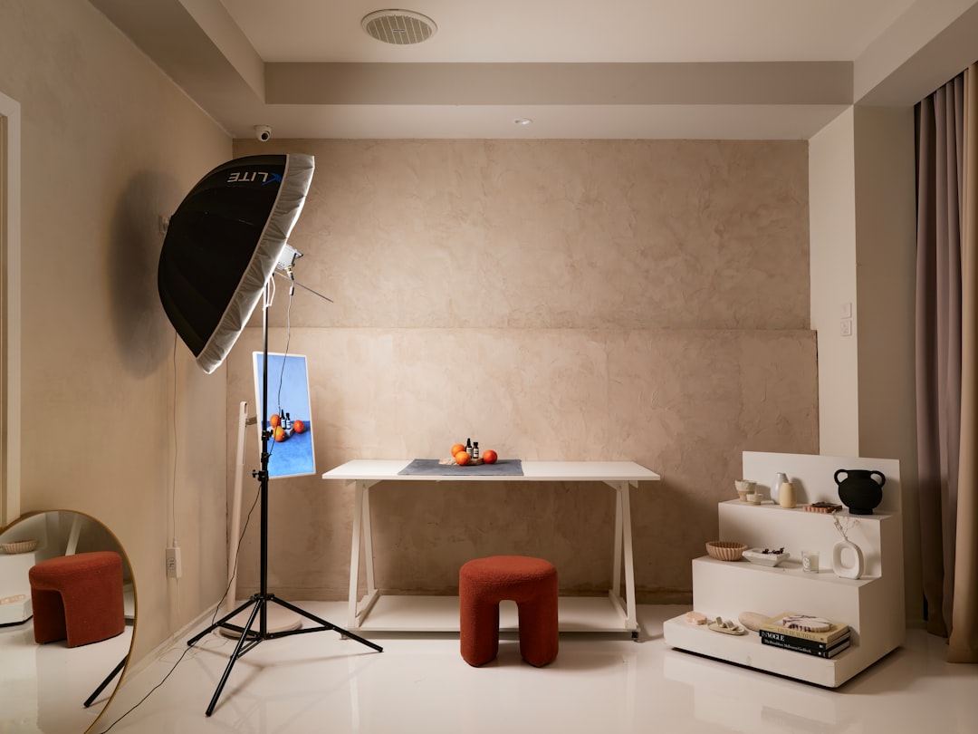 A photography studio setup with a white table, a red stool, and a mirror, illuminated by a large black light.