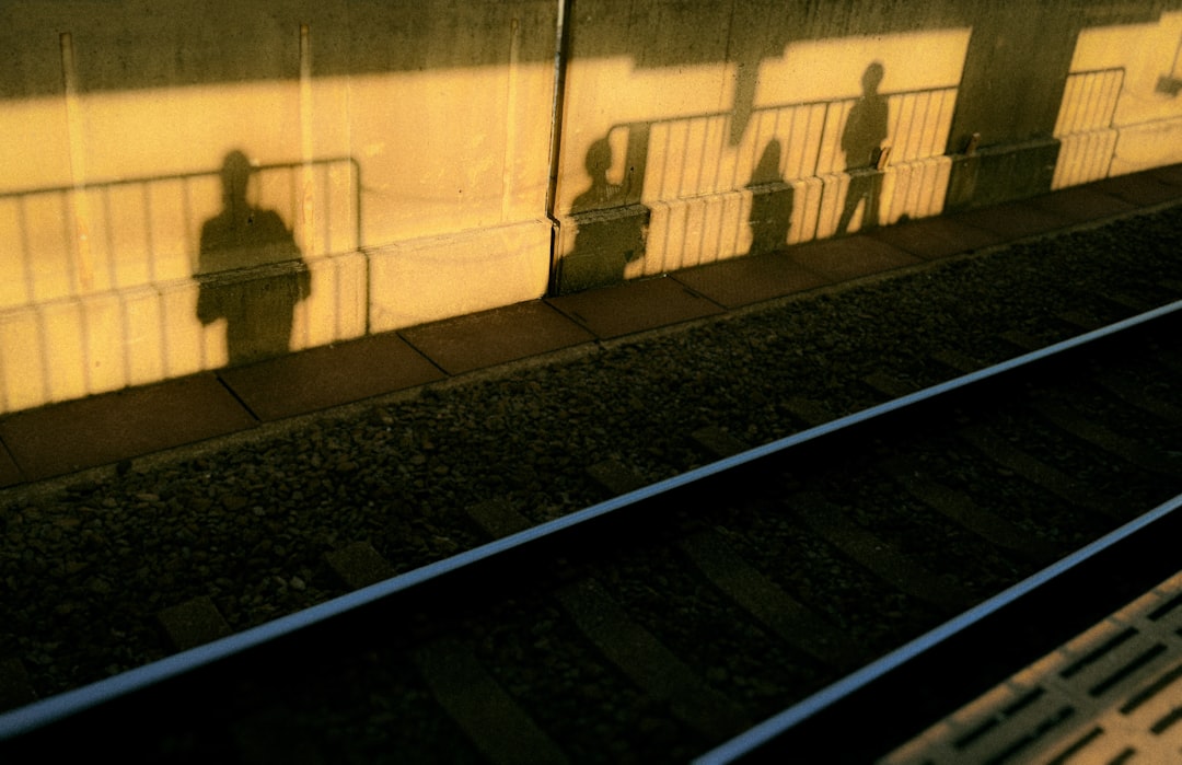 A shadowy figure stands on a platform, casting a silhouette against a wall, with a train track stretching out in the foreground.