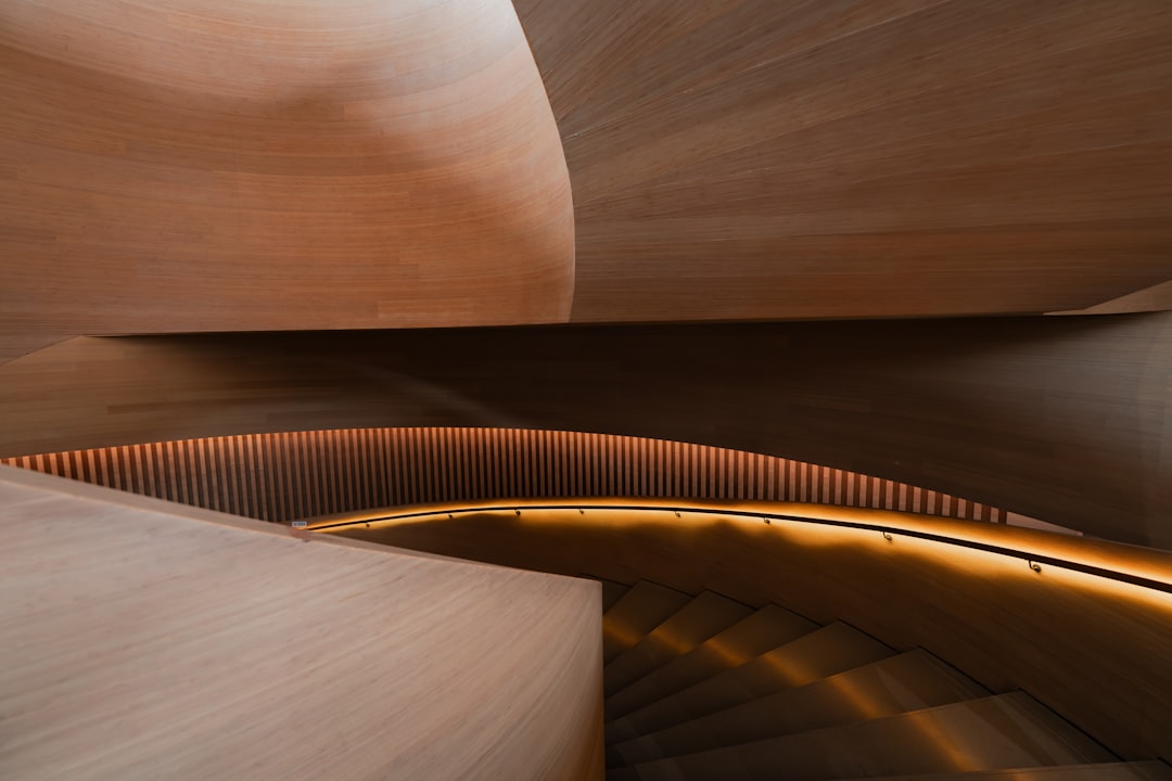 A wooden staircase with a curved railing and a wall of wooden slats behind it, illuminated by warm lighting.