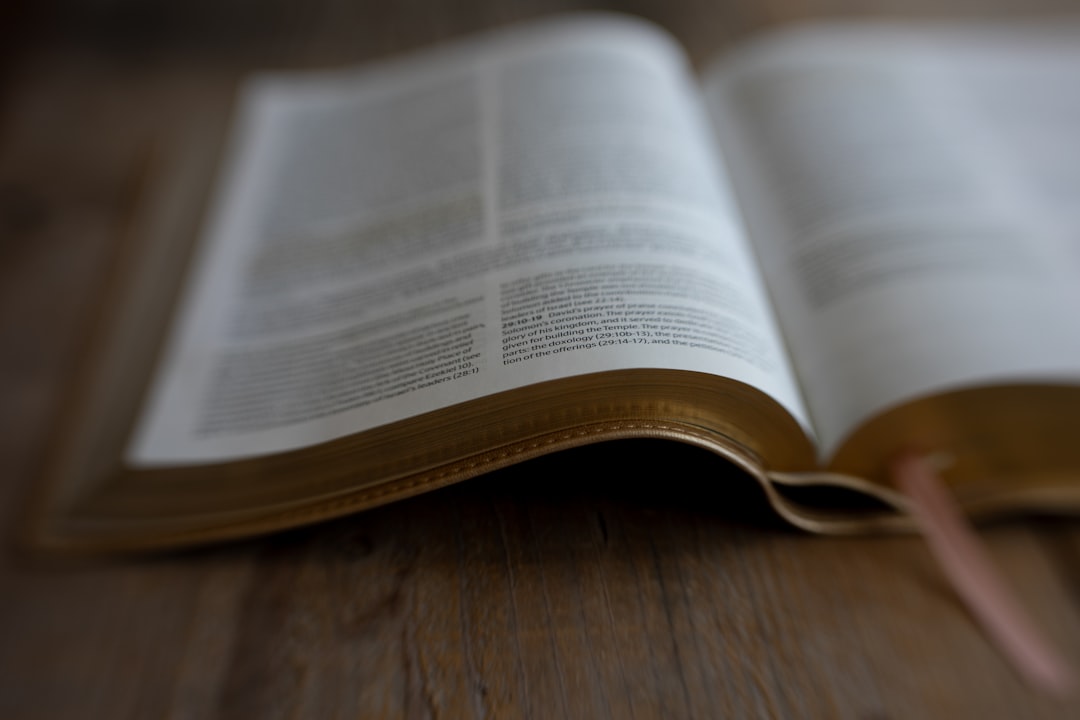 A Bible lies open on a wooden surface, its pages slightly curled and worn, with a pink bookmark peeking out from the right page.