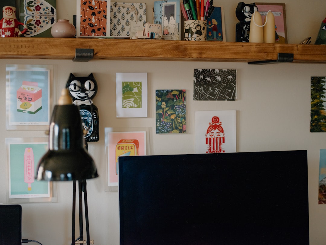 A wooden shelf with a black lamp and a computer monitor in front of it, surrounded by colorful artwork on the wall.