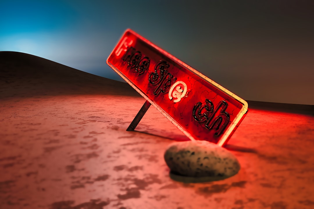 A red sign, tilted at an angle, reads "No Trespassing" in black letters, resting on a rock in the desert.