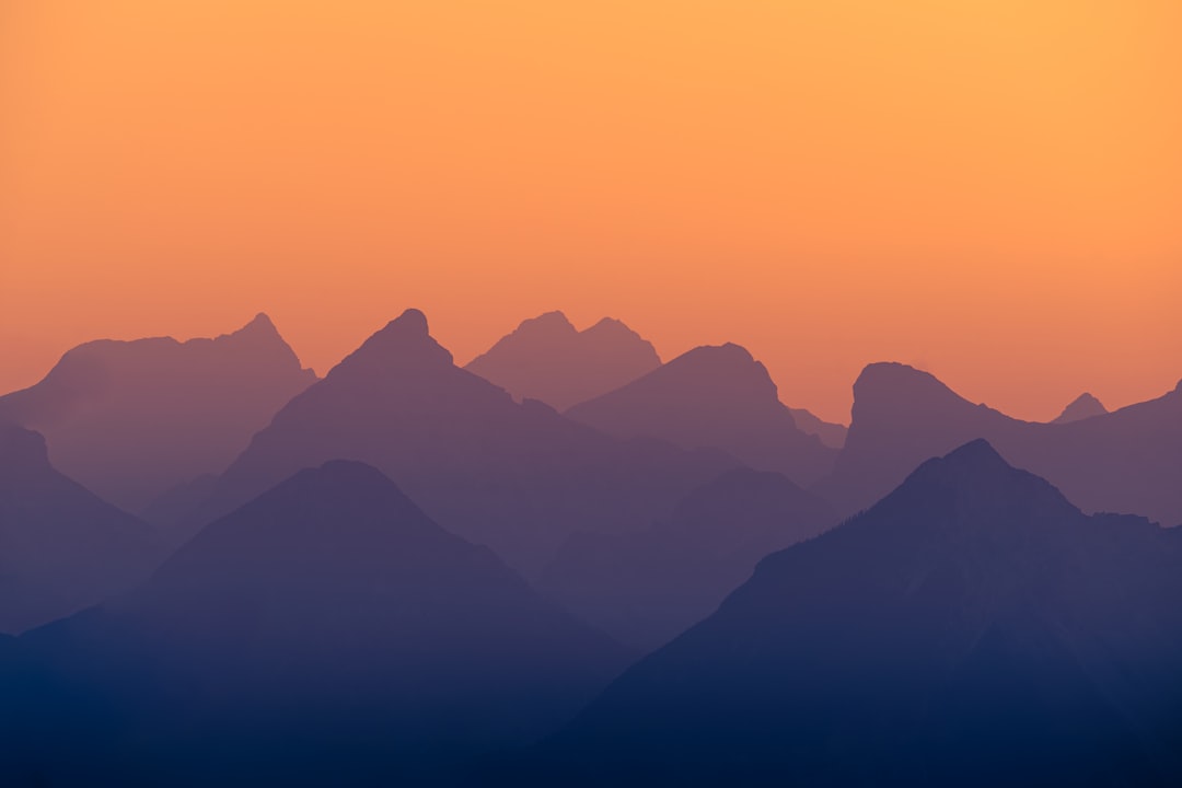 Majestic mountains silhouette against a vibrant orange and yellow sunset sky.