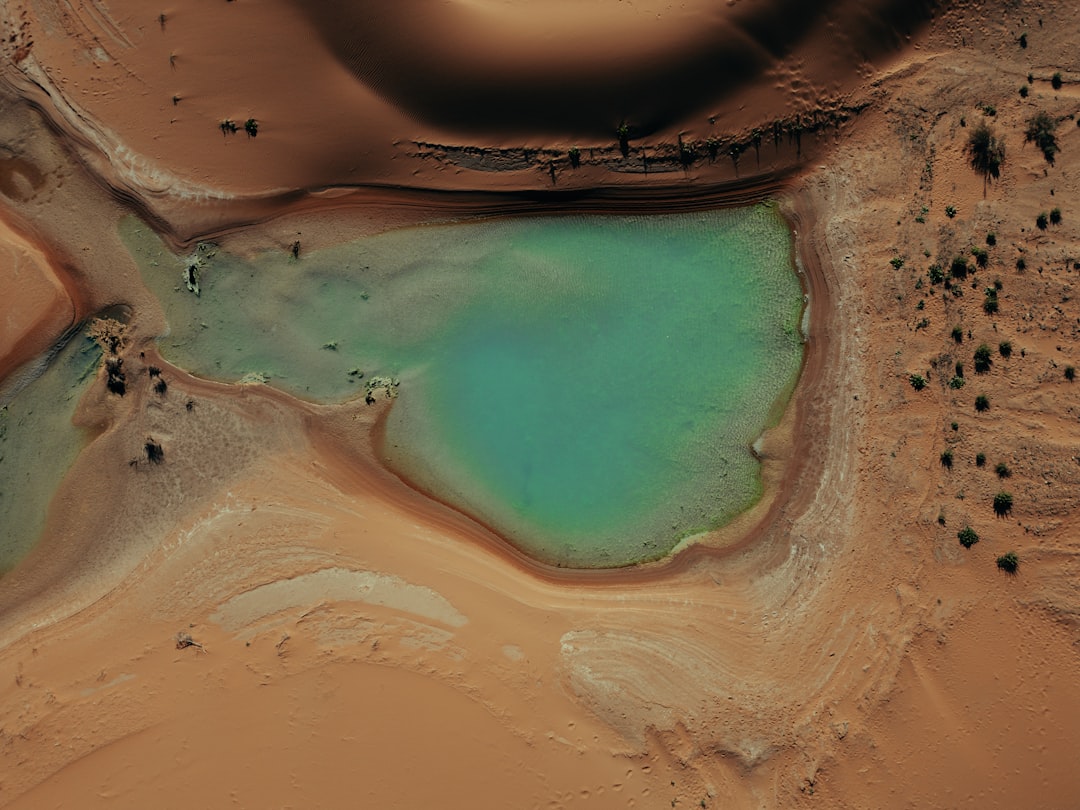 A vast desert landscape unfolds, with a striking turquoise-colored body of water nestled among the sandy dunes.
