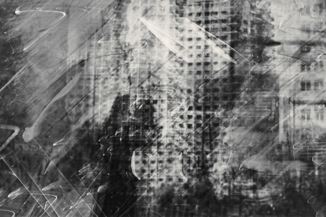 A cityscape with tall buildings and a street is captured in a black-and-white photograph with a blurred and abstract quality.