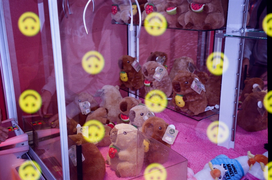 A collection of brown teddy bears with watermelon slices and smiling faces sit in a glass case, surrounded by a vibrant pink carpet and a subtle yellow smiley face pattern.