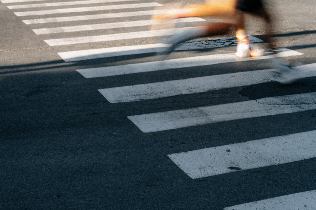 A person's legs are blurred as they cross a crosswalk, likely in a hurry.