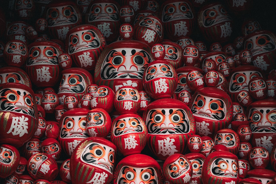 A collection of red Daruma dolls with white faces and black eyebrows.