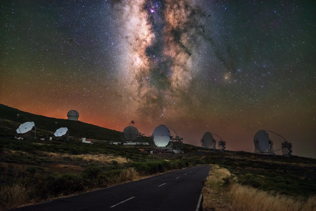 A serene landscape unfolds, with a road winding through a field of grass, set against a backdrop of rolling hills and a starry night sky.