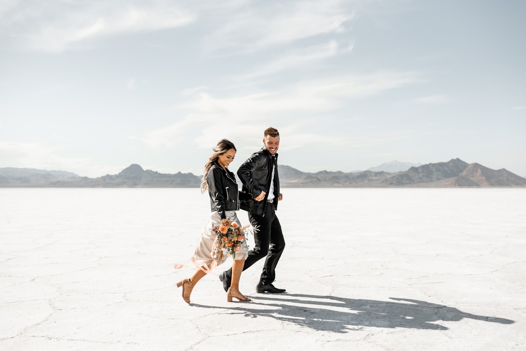 A couple walks hand in hand across a vast, flat expanse of white salt, their shadows stretching out behind them.