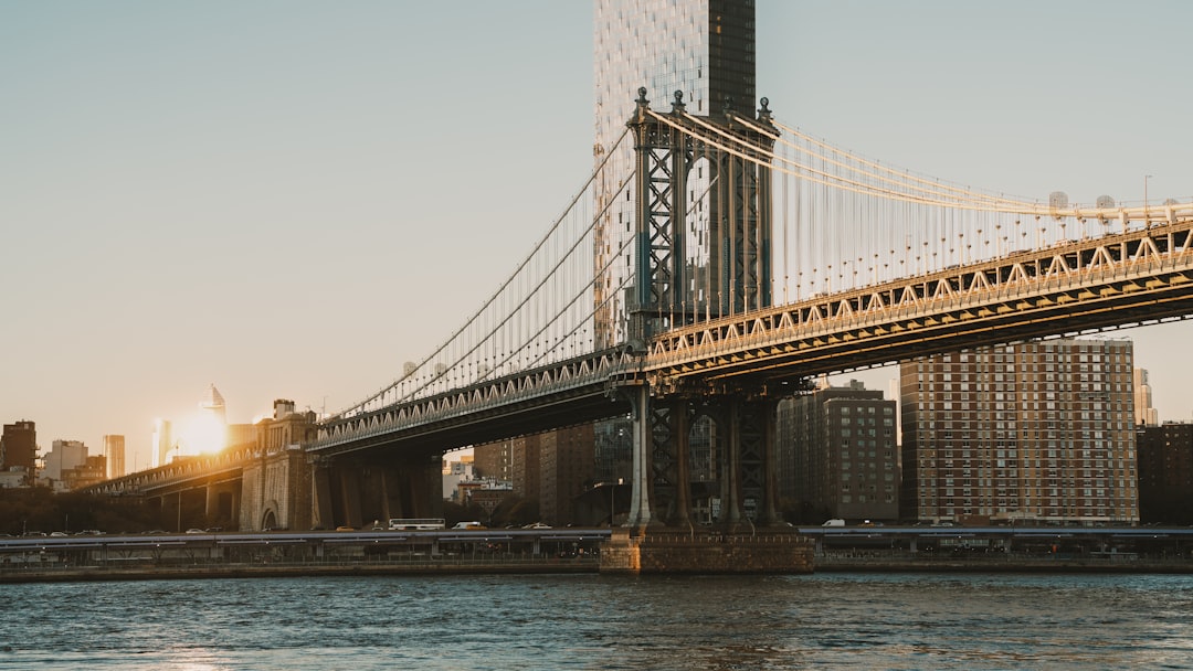 A majestic suspension bridge spans the river, its metal structure gleaming in the sunlight.